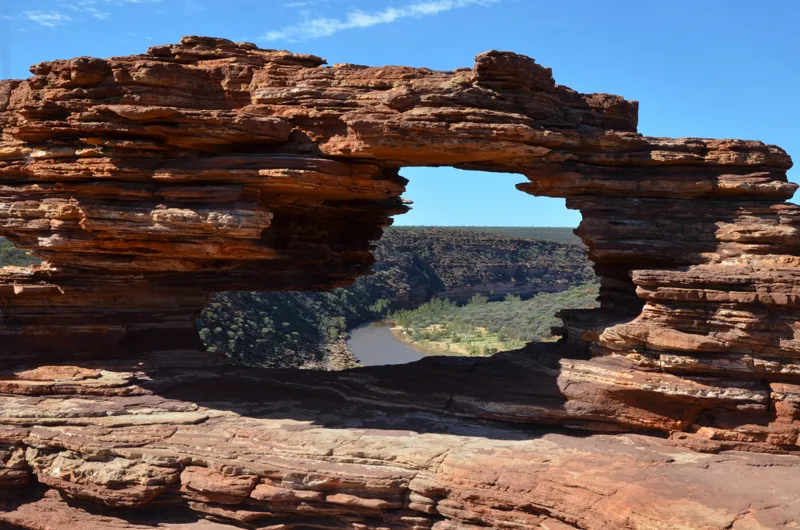 A natural opening through layered red rock beneath a blue sky.